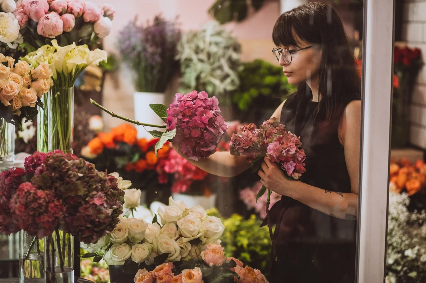 Florist arranging pink hydrangeas and roses in a flower shop