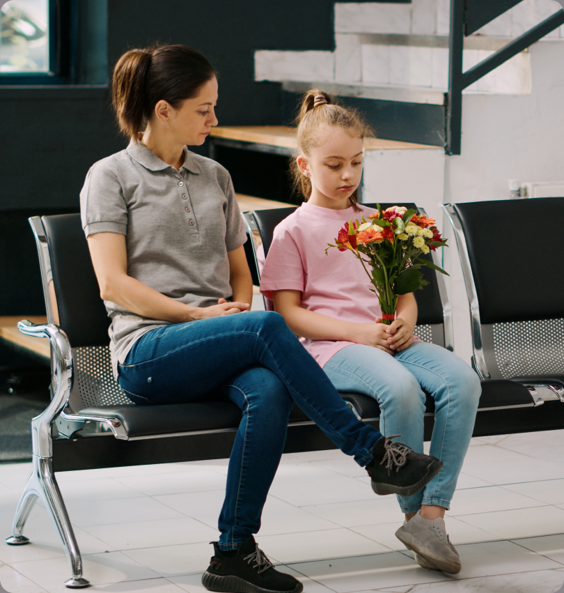 Parent and child seated in a hospital waiting room with flowers